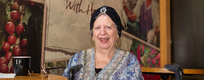 An elderly lady sits, smiling in a cafe